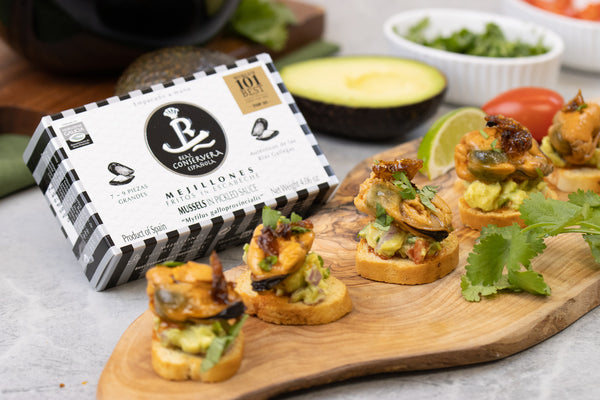 Mussel Bocaditos on a Charcuterie Board with a box of Award Winning Real Conservera Espanola of Mussels next to it. Avocado, Cilantro & Lime in the Background.